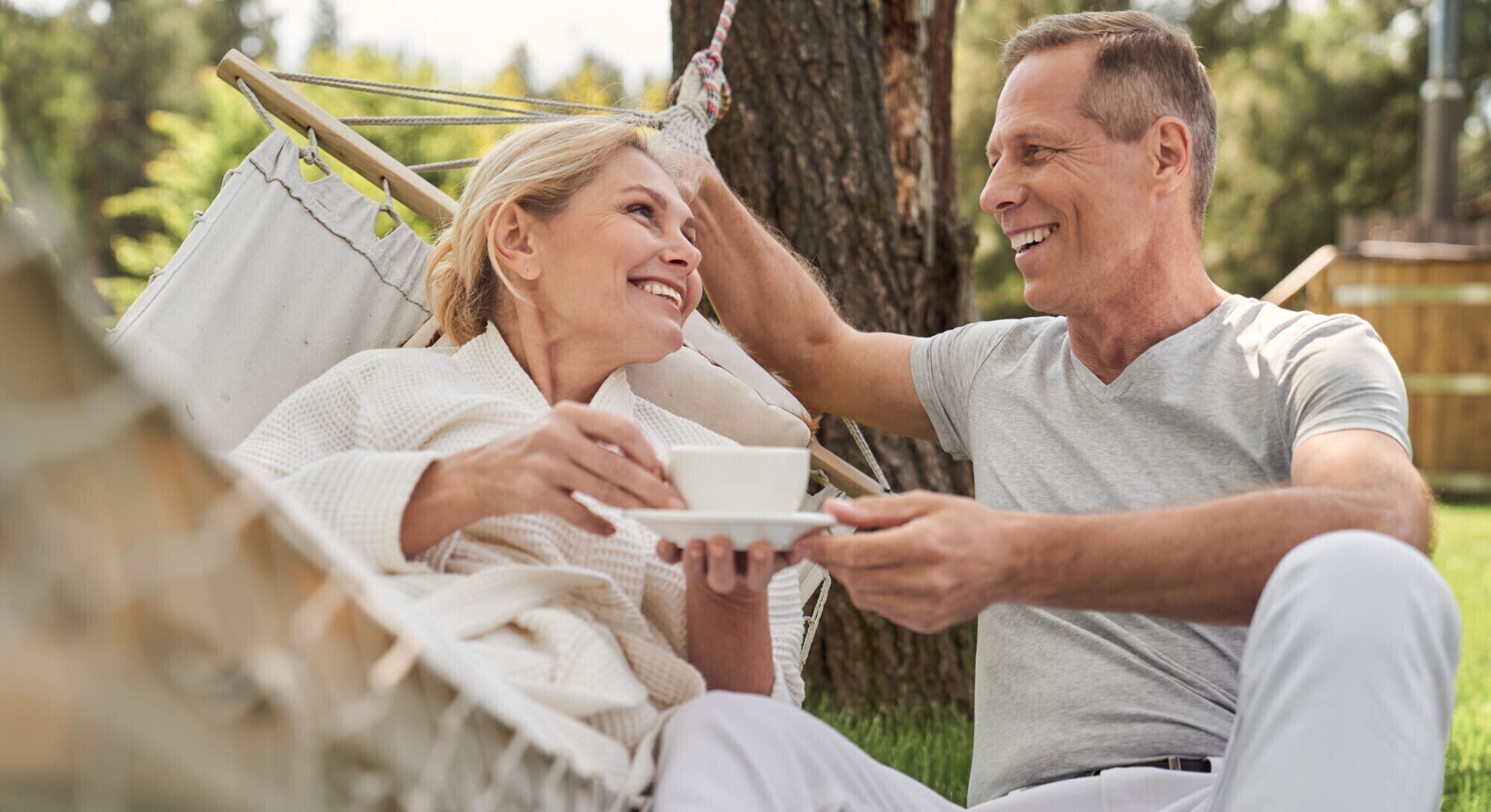 A woman lying in a hammock with a cup of tea talks to her husband